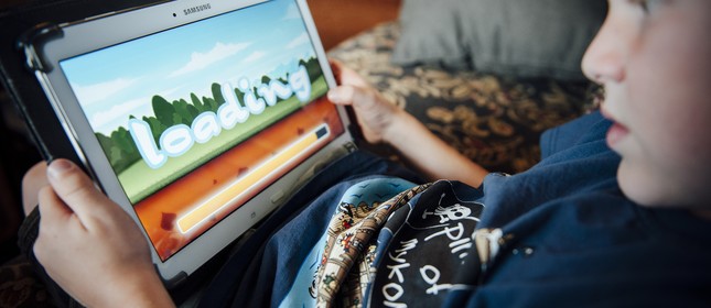 Criança aguarda o término do download de um jogo on-line em um tablet