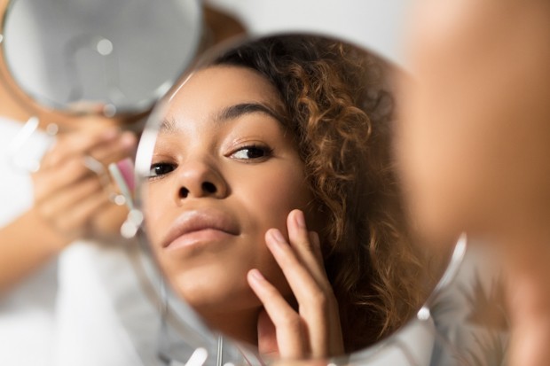 Skincare Concept. Afro Woman Looking In Mirror Touching Face And Perfect Skin At Bathroom. Selective Focus (Foto: Envato)