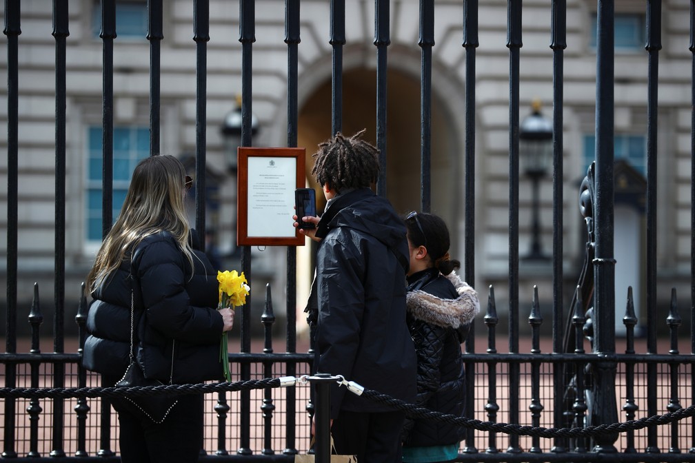 Pessoas observam e tiram foto do aviso no portão do Palácio de Buckingham que anuncia a morte do príncipe Philip, marido da Rainha Elizabeth II, em 9 de abril de 2021 — Foto: Hannah McKay/Reuters