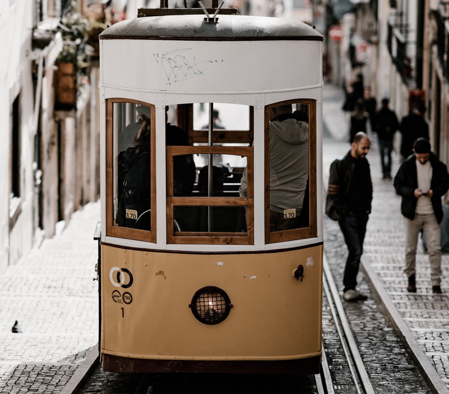 Lisboa: homens caminham ao lado de bondinho e um deles consulta telefone