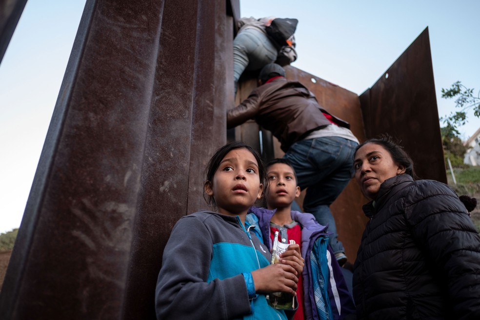 Migrantes da América Central sobem a cerca da fronteira México-EUA enquanto outros hesitam. Registro foi feito na quarta-feira (12) 