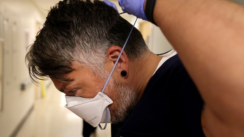 Profissional de saúde ajustando máscara N95/PFF2 atrás da cabeça; uma boa vedação pode garantir que todo o ar inspirado seja filtrado (Foto: Getty Images via BBC News)
