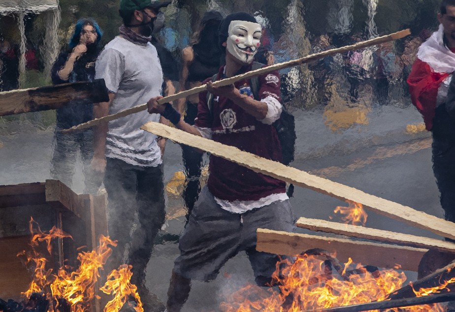 Uma manifestante joga uma ripa de madeira em uma barricada em flamas durante protestos em Santiago, no Chile