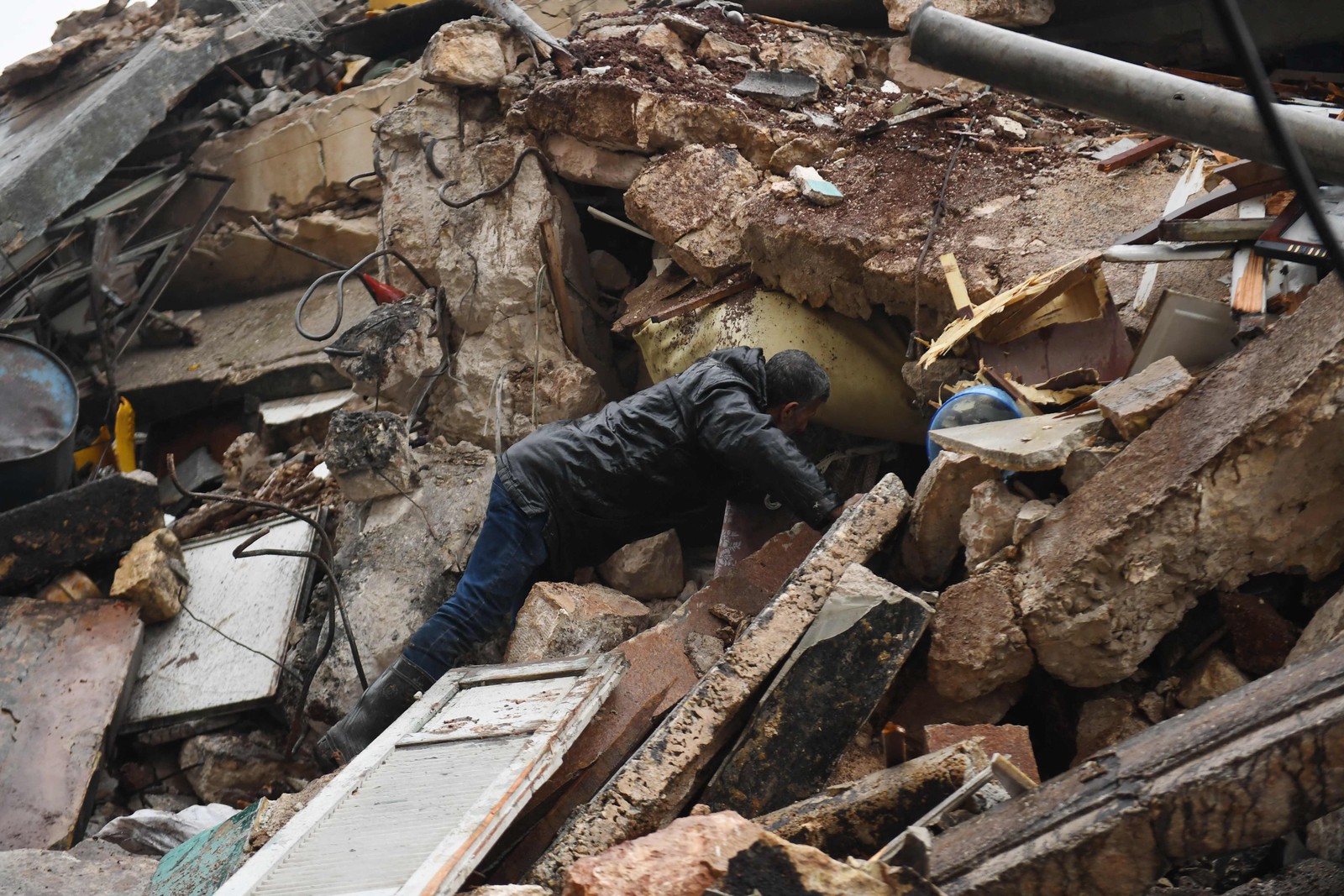 Homem procura sobreviventes sob os escombros de um prédio que desabou na cidade de Aleppo. Terremoto de magnitude 7,8 atingiu a Turquia e a Síria, matando centenas de pessoas.  — Foto: AFP