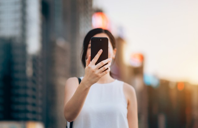 Young woman using smartphone outdoors in front of blurry city scene (Foto: Getty Images)