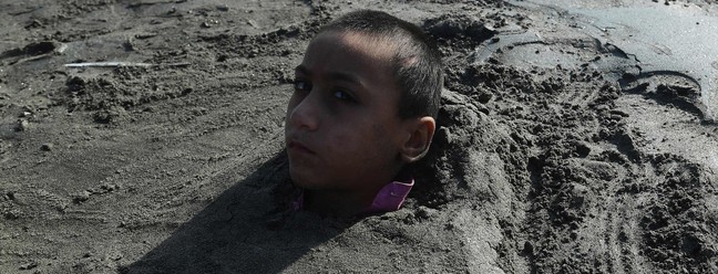 Menino é coberto de areia em uma praia por seus pais sob a crença de que a exposição durante um eclipse solar curará sua doença, em Karachi, Paquistão — Foto: ASIF HASSAN/AFP