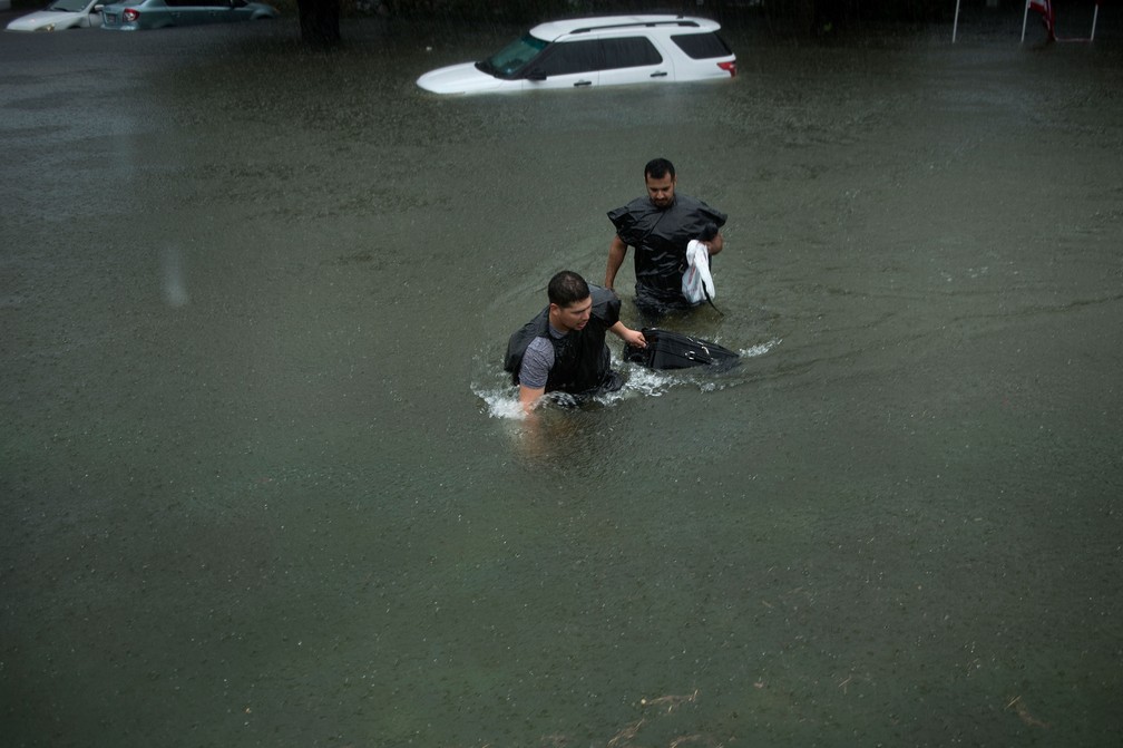 Moradores carregam seus pertences no meio da inundação em Galveston, Texas, neste domingo (27) (Foto: Brendan Smialowski/AFP )