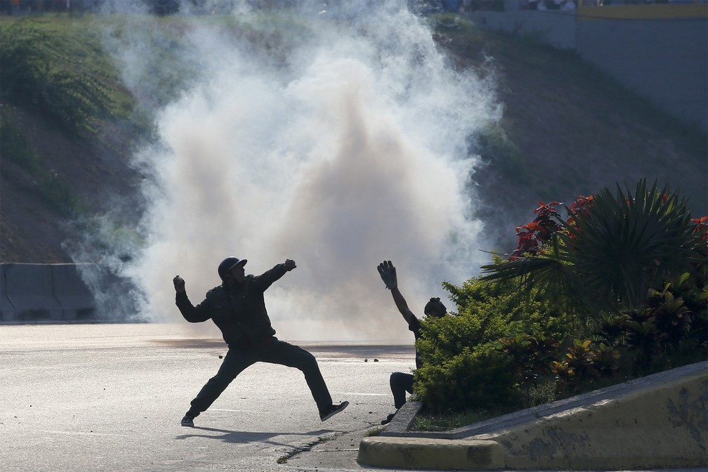 Diante de gás-lacrimogêneo, manifestantes atiram pedras contra forças leais a Nicolás Maduro diante da base aérea 'La Carlota', em Caracas — Foto: Fernando Llano/AP