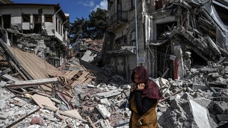 Mulher caminha próximo a escombros de prédios desabados em Hatay, um mês depois do terremoto que matou 46 mil entre Turquia e Síria — Foto: OZAN ​​KOSE/AFP
