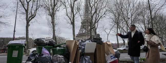 Pessoas passam por lixo não coletado perto da Torre Eiffel, em Paris, em imagem do dia 12 de março de 2023 — Foto: Michel Euler/AP