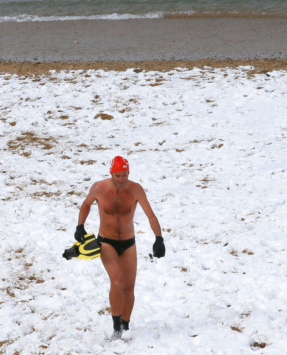 Nadador caminha em praia coberta de neve em Biarritz, na França, nesta quarta-feira (28)  (Foto: Bob Edme/ AP)