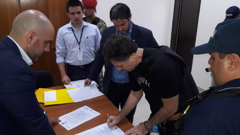 Bruno Farina assina documento pouco antes de ser enviado de volta ao Brasil  — Foto: Divulgação/Polícia Nacional do Paraguai