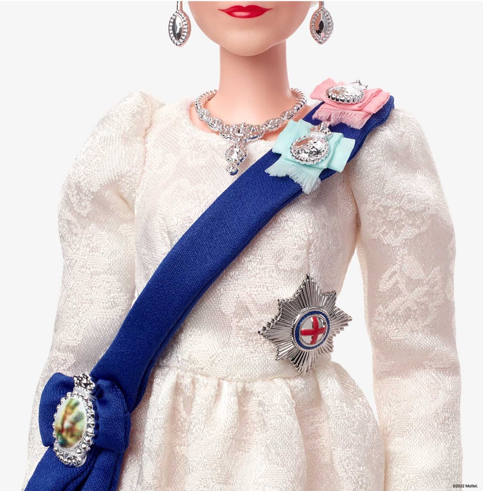A boneca vem com um vestido marfim com uma fita azul e apresenta detalhes do passado do monarca — Foto: Mattel Creations