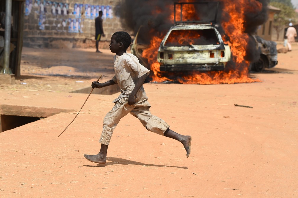 22 de fevereiro - Uma criança corre enquanto carros são incendiados após confrontos entre os partidários do All Progressives Congress (APC) e do Partido Democrático Popular (PDP), de oposição, em Kofa, no norte da Nigéria — Foto: Pius Utomi Ekpei/AFP
