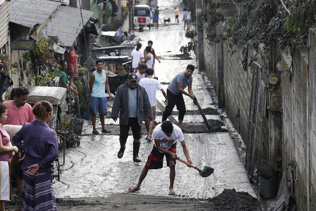 Moradores removem camada de cinzas vulcânicas acumuladas em frente a suas casas em Tagaytay, província de Cavite, após o vulcão Taal expelir uma enorme nuvem de cinzas nas Filipinas — Foto: Aaron Favila/AP