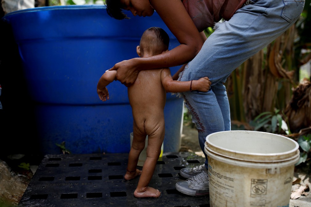 Mãe em situação de pobreza dá banho em filho na Venezuela: ao menos 22% das crianças menores de 5 anos sofrem de desnutrição crônica no país — Foto: Carlos García Rawlins/Arquivo/Reuters