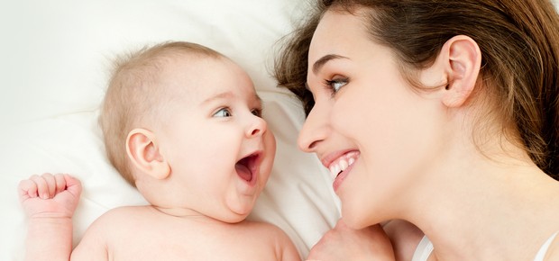 Bebê rindo na cama com a mãe (Foto: Shutterstock)