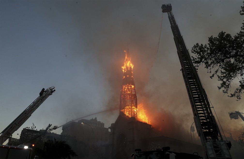 Bombeiros tentam conter o fogo na Igreja La Asunción, incendiada por vândalos encapuzados durante protesto em Santiago, no Chile — Foto: Esteban Felix/AP