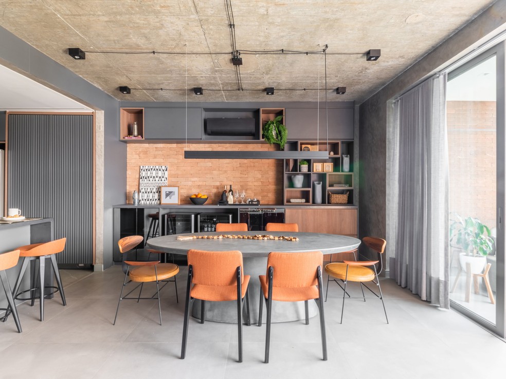 DÚPLEX DE RAFAEL: Detalhe da área de refeições com cadeiras variadas e texturas diversas - incluindo os tijolos aparentes, típicos do estilo industrial — Foto: Guilherme Pucci