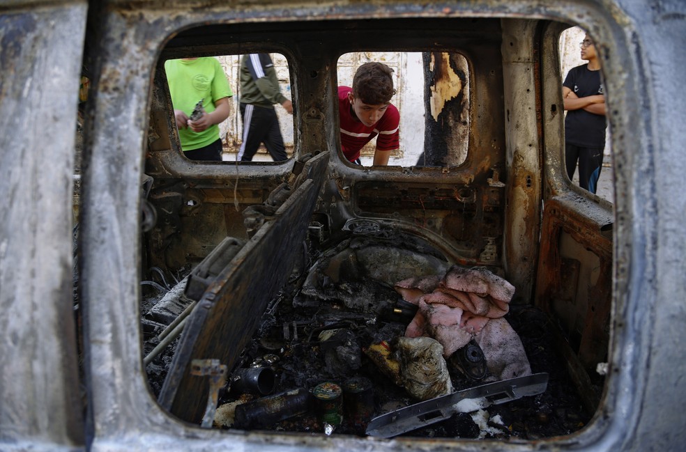 Crianças palestinas olham para carro destruído após ser atingido em ataque aéreo israelense na Cidade de Gaza na quarta (19) — Foto: Hatem Moussa/AP