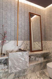 No apartamento reformado por Maicon Antoniolli, o lavabo é revestido de mármore estatuário até metade da parede. Na parte superior, papel de parede trazido de viagem. Espelho com moldura de pau-ferro