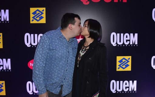 Jiang Pu e o marido, Ricardo Matioli, se beijam em frente ao painel de QUEM e Banco do Brasil