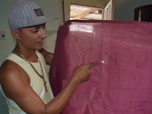 O filho de dona Neta mostra a marca na cortina da casa feita pelo tiro que matou sua mãe  (Foto: André Resende/G1)