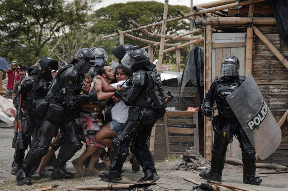 Policiais prendem um homem enquanto sua esposa e família resistem, durante despejos de pessoas do assentamento de San Isidro, em Puerto Caldas, Risaralda, Colômbia, em 6 de março de 2021 — Foto: Vladimir Encina