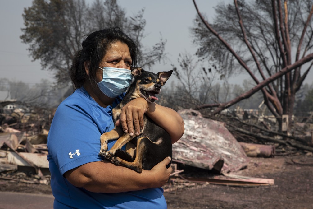 Mulher que teve trailer onde morava destruído por incêndio no Oregon segura um cachorro enquanto conta os danos do fogo nesta quinta (10) — Foto: Paula Bronstein/AP Photo