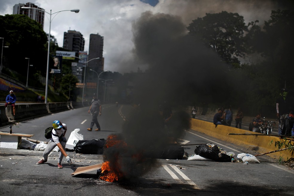 Manifestante incendia pneu para bloquear rua nesta quarta-feira (26) na Venezuela (Foto: REUTERS/Carlos Garcia Rawlins)