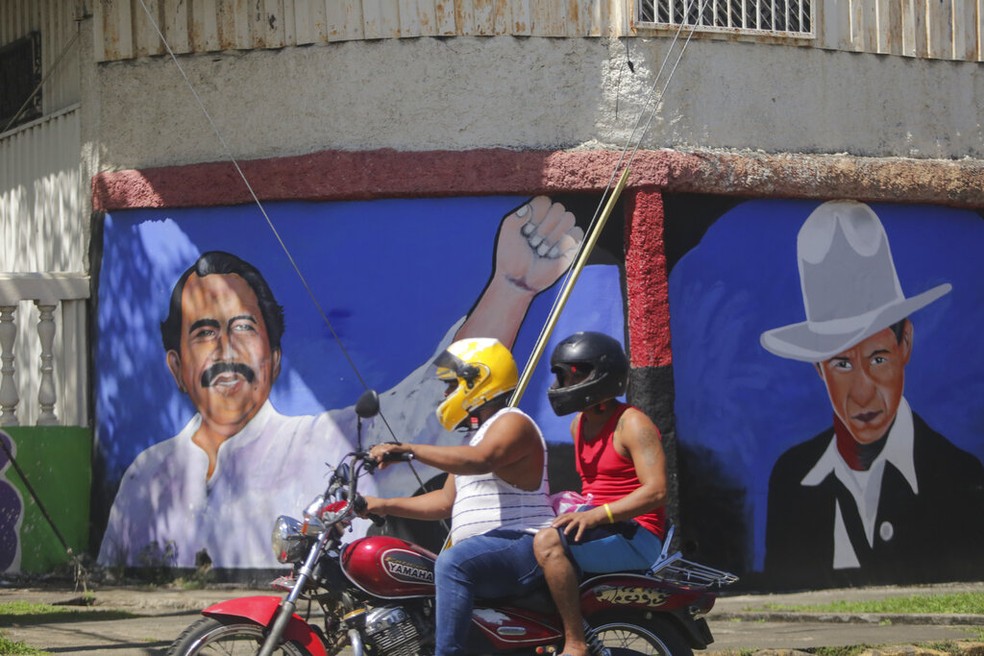 Motociclista passa diante de mural com o rosto de Daniel Ortega, presidente da Nicarágua (à esquerda), e do revolucionário César Augusto Sandino, durante as eleições gerais deste domingo (7), em Manágua — Foto: Andrés Nunes/AP Photo