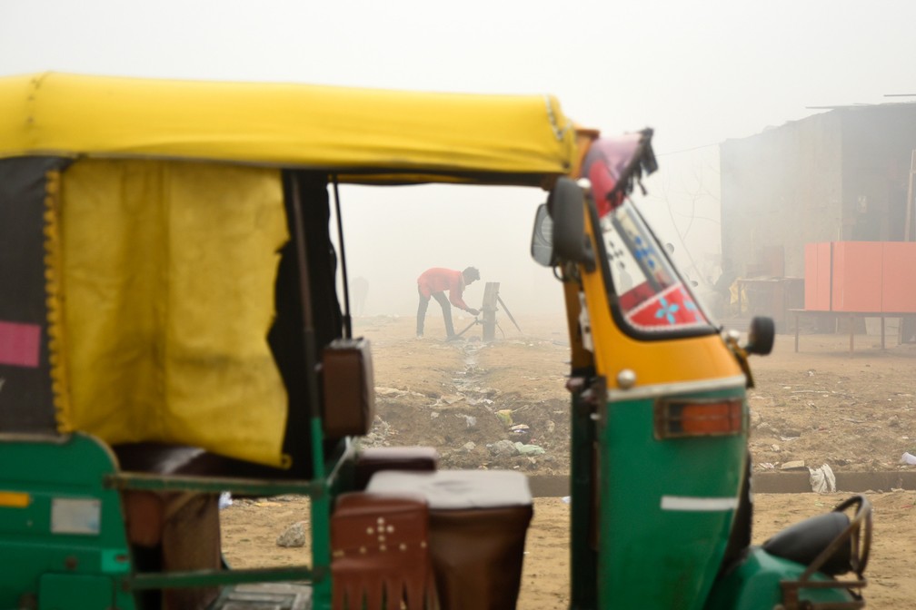 Um jovem lava as mãos usando a água de uma bomba manual ao lado de um riquixá estacionado em Greater Noida, perto de Nova Delhi, na Índia. Durante o inverno, uma névoa espessa envolve a maior parte do norte do país, causada pela poeira, queima de plantações, emissões das fábricas e pela queima de carvão e pilhas de lixo  — Foto:  R S Iyer/AP