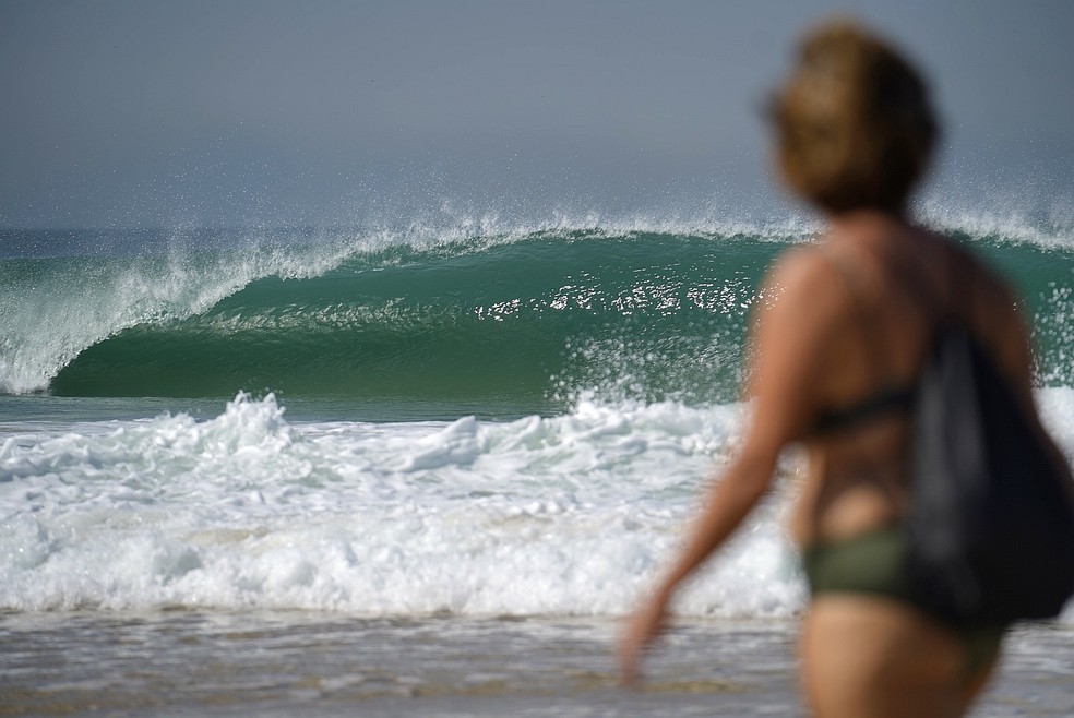 Mulher caminha na praia do Leme com uma onda tubular quebrando ao fundo em 2020 — Foto: Marcos Serra Lima/G1