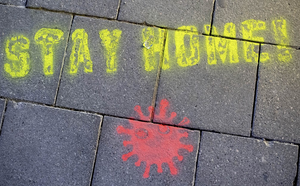 16 de março - 'Fique em casa!', diz a frase em estêncil pintada com uma representação do coronavírus no chão de uma praça em Munique, na Alemanha — Foto: Sven Hoppe/DPA via AP