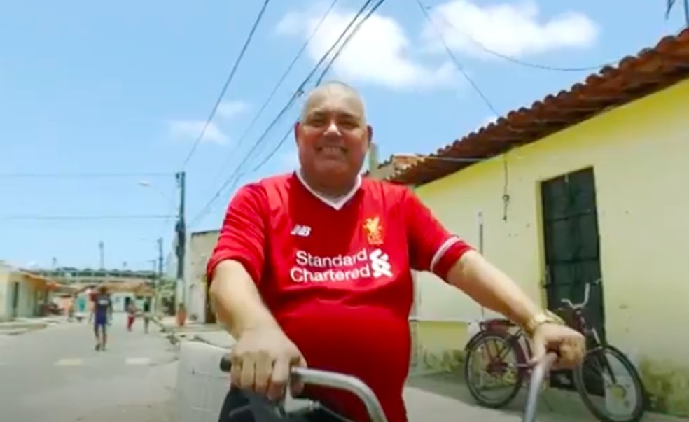 O pai de Firmino é José de Oliveira, ex-vendedor ambulante nas ruas do Trapiche, com a camisa do Liverpool — Foto: Reprodução Jornal Nacional