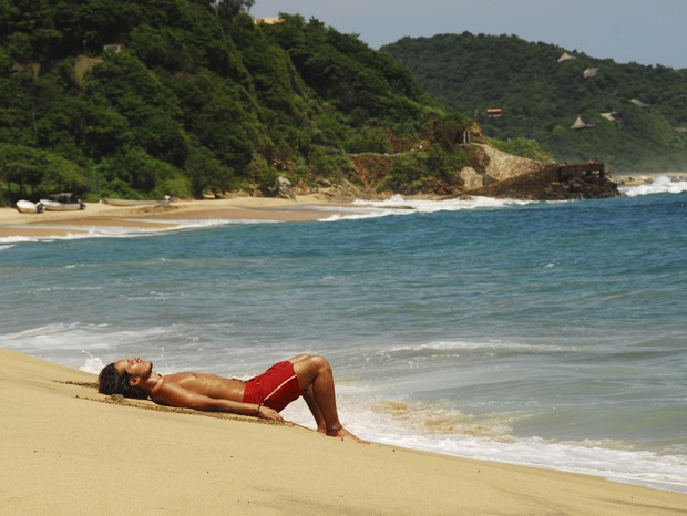 Mexico, Mazunte, view of a shirtless man relaxing on sand at the shore of the beach with green mountains in the background (Foto:  )
