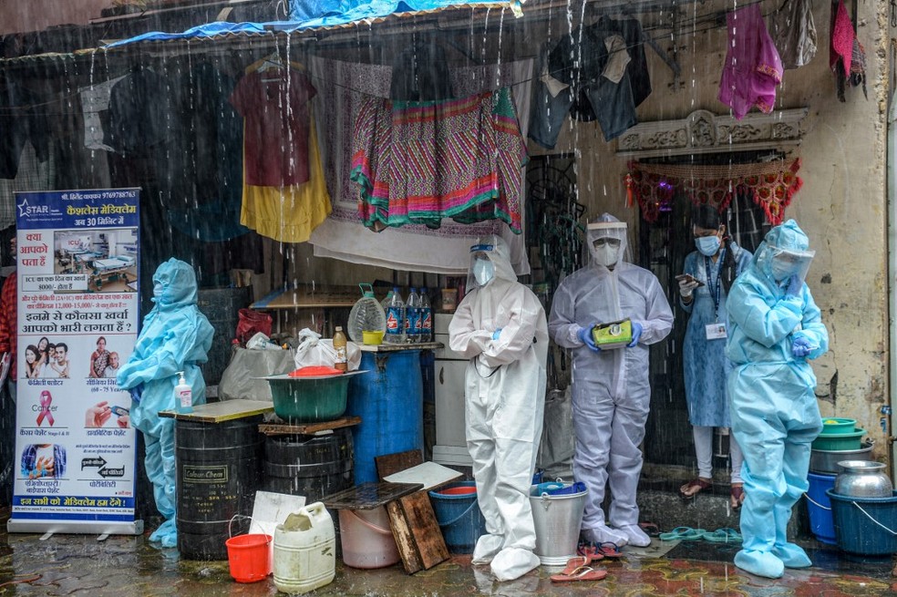 Profissionais de saúde usando equipamentos de proteção individual (EPIs) se abrigam da chuva enquanto fazem rastreio de Covid-19 em Mumbai, na Índia, nesta quarta-feira (12).  — Foto: Indranil Mukherjee / AFP