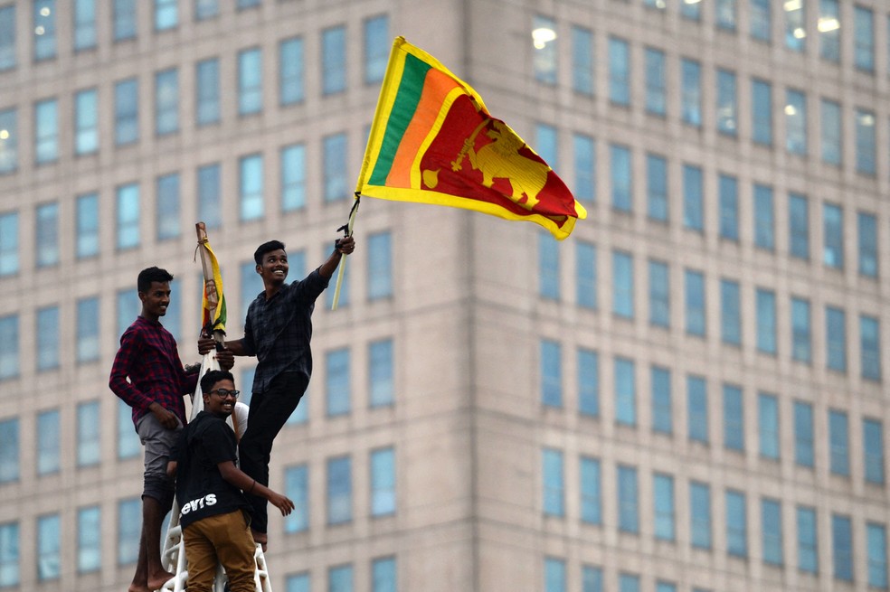 11/07 - Um homem agita a bandeira nacional do Sri Lanka depois de escalar uma torre perto da secretaria presidencial em Colombo, capital do país, invadida por manifestantes contra o governo — Foto: Arun Sankar/AFP