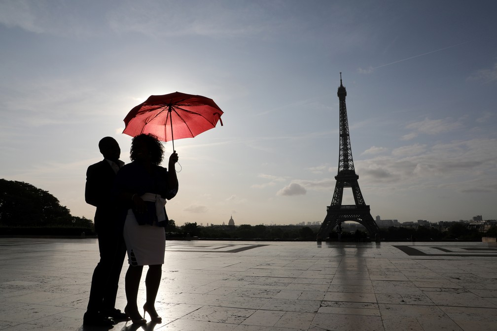 Um casal com um guarda-chuva vermelho observa o nascer do sol na Praça do Trocadero, perto da Torre Eiffel, em Paris, na França (Foto: Ludovic Marin/AFP)