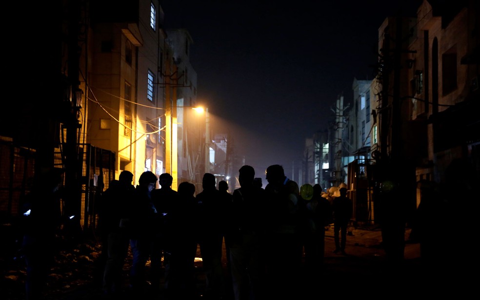 Policiais e agentes de segurança são vistos do lado de fora de depósito incendiado em Nova Déli, na Índia, no domingo (21, horário local) (Foto: AP Photo/Altaf Qadri)
