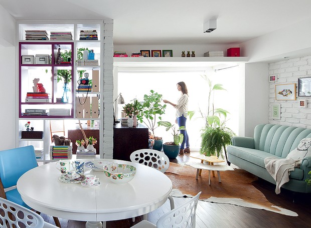 O apartamento tem apenas 70 m², mas a sala é ampla, com poucos e pequenos móveis. A prateleira no alto oferece mais espaço para guardar livros e expor quadros da arquiteta Marcela Madureira. Como tudo é branco, o elemento passa quase despercebido (Foto: Maíra Acayaba/Casa e Jardim)