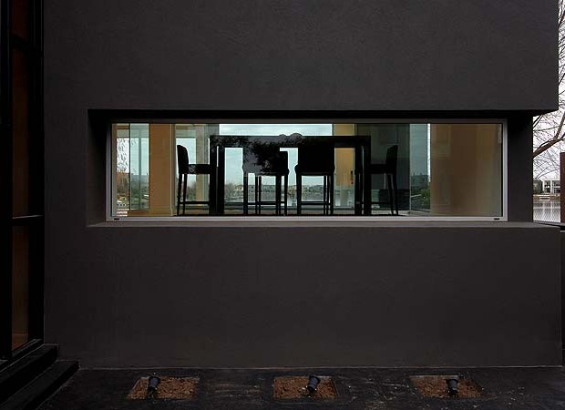 Um rasgo com vidro fixo na fachada principal dá uma visão da sala de jantar, que fica em patamar mais alto em relação à garagem na frente da casa (Foto: Daniela Mac Adden/Surpressagency.com )