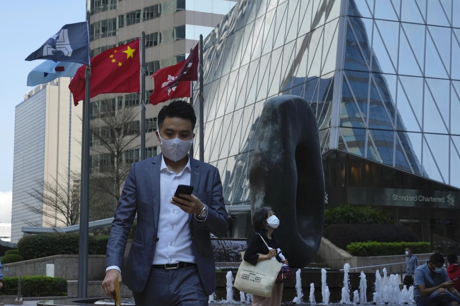 A man wearing a face mask walks though the towering skyscrapers in the Central district of Hong Kong, Monday, March 14, 2022. China’s mainland is seeing a widespread surge of new infections across its