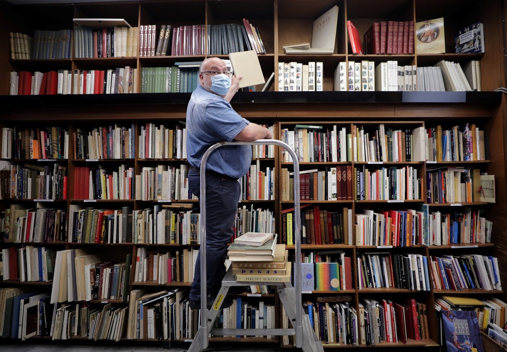 Homem usando máscara de proteção organiza livros na livraria La Sorbonne, na França — Foto: Eric Gaillard/Reuters