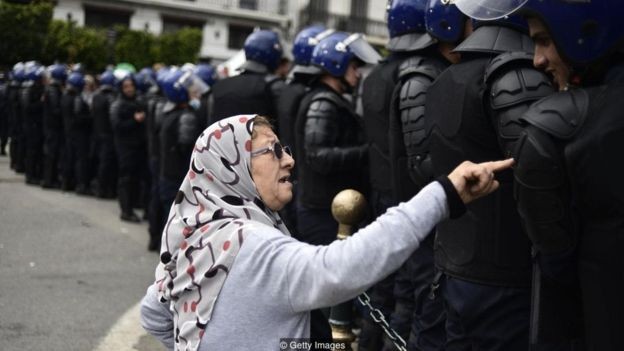 Uma senhora conversa com membros das forças de segurança durante os recentes protestos contra o governo na Argélia (Foto: Getty Images via BBC News)