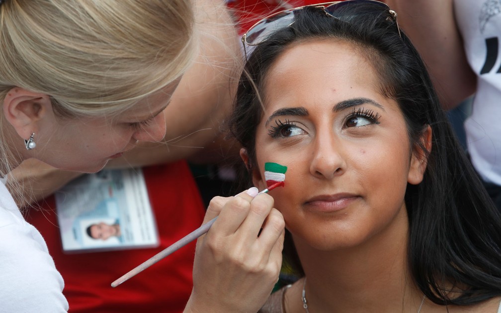 Mulher pinta rosto de torcedora iraniana em estádio de São Petersburgo durante jogo entre Irã e Marrocos na Copa do Mundo da Rússia, na sexta-feira (15) — Foto: AP Photo/Dmitri Lovetsky