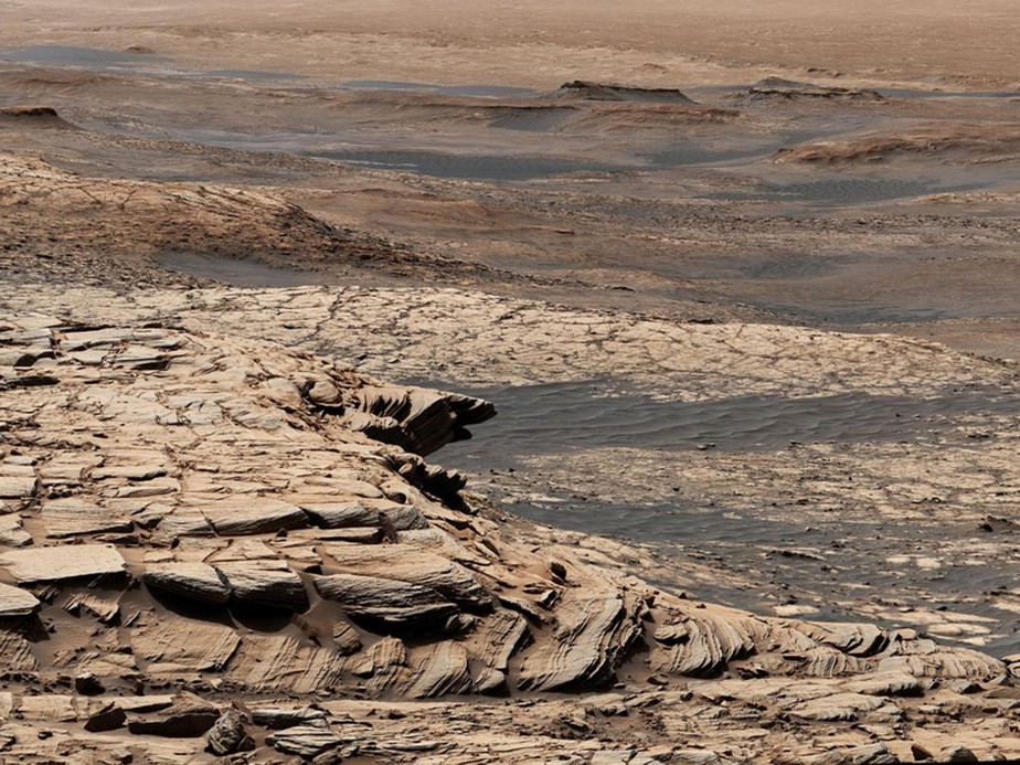 Feita a partir de 28 imagens, esta visão do rover Curiosity Mars da Nasa foi capturada depois que o robô subiu a encosta íngreme de uma característica geológica chamada 'Greenheugh Pediment'. Ao longe, na parte superior da imagem, está a Cratera Gale, que fica perto da região Aeolis Dorsa, que os pesquisadores acreditam ter sido um oceano
