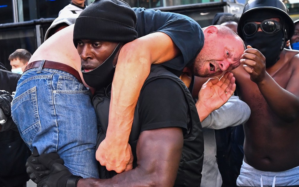 O manifestante negro Patrick Hutchinson carrega um contra-manifestante branco ferido para local seguro, perto da estação Waterloo, em Londres, durante protesto pela morte de George Floyd, no sábado (13) — Foto: Reuters/Dylan Martinez 