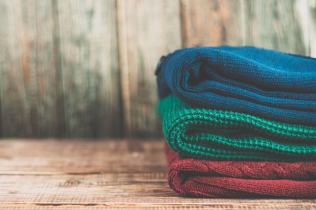 Warm clothes laid in a pile on wooden background.Colorful sweaters on a wooden table. (Foto: Getty Images/iStockphoto)