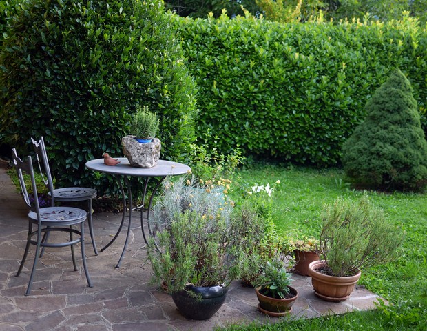 Idyllic springtime patio in Italian garden with small wrought iron table and chairs against dark laurel hedge. A selection of kitchen herbs in pots. (Foto: Getty Images)